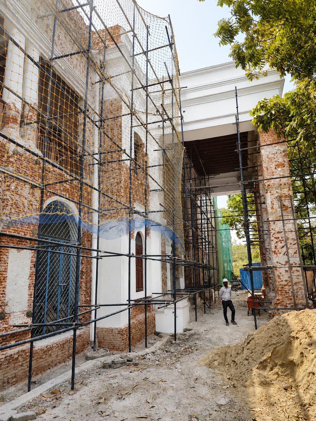 Facade — brick masonry exposed mid-repair, scaffolding and safety netting